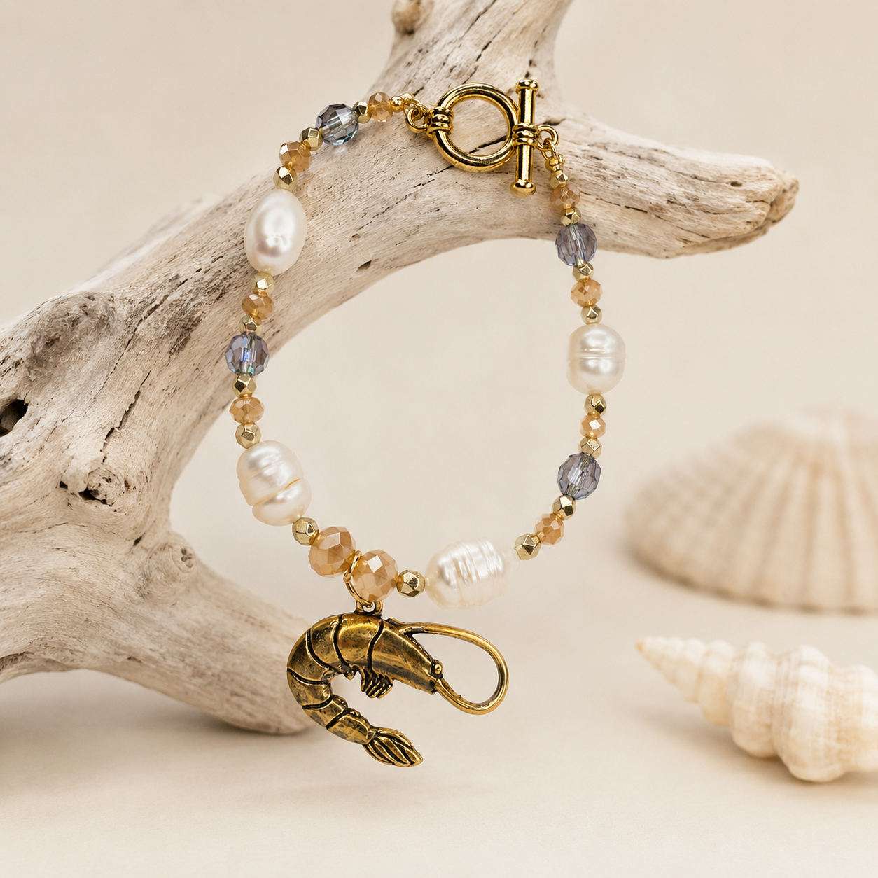 Bayou Shrimp Pearl Bracelet with freshwater pearls, faceted glass beads, antique-gold shrimp charm, and toggle clasp displayed over pale driftwood with coastal accents.